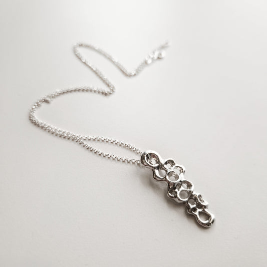 Slim Raíz Necklace, sculptural silver pendant symbolizing resilience and inner strength.
Collar Raíz Slim, colgante escultural en plata que simboliza resiliencia y fuerza interior.