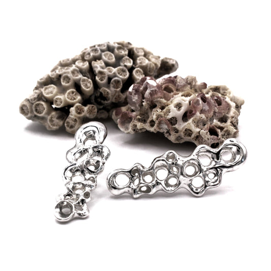 Silver coral-shaped jewelry pieces on a white background. Raíz Long Earrings in recycled sterling silver 925, asymmetrical barnacle-inspired statement earrings by Naturalesa Jewelry.