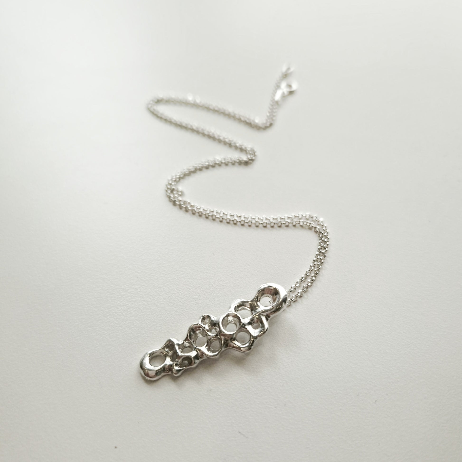 Silver necklace with a unique pendant on a white background.Raíz Slim Pendant in recycled sterling silver 925 with diamond rolo chain, minimalist sea inspired necklace. Colgante Raíz Slim en plata reciclada 925 con cadena rolo diamante, collar minimalista inspirado en el mar.